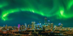 Downtown Edmonton skyline at night illuminated by vibrant green Northern Lights.